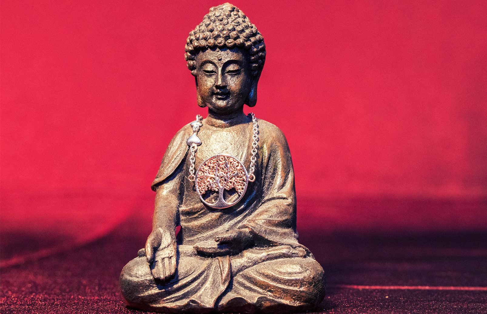 Produktfoto eines Lebensbaum-Armbands auf einer kleinen Buddha-Statue mit rotem Hintergrund